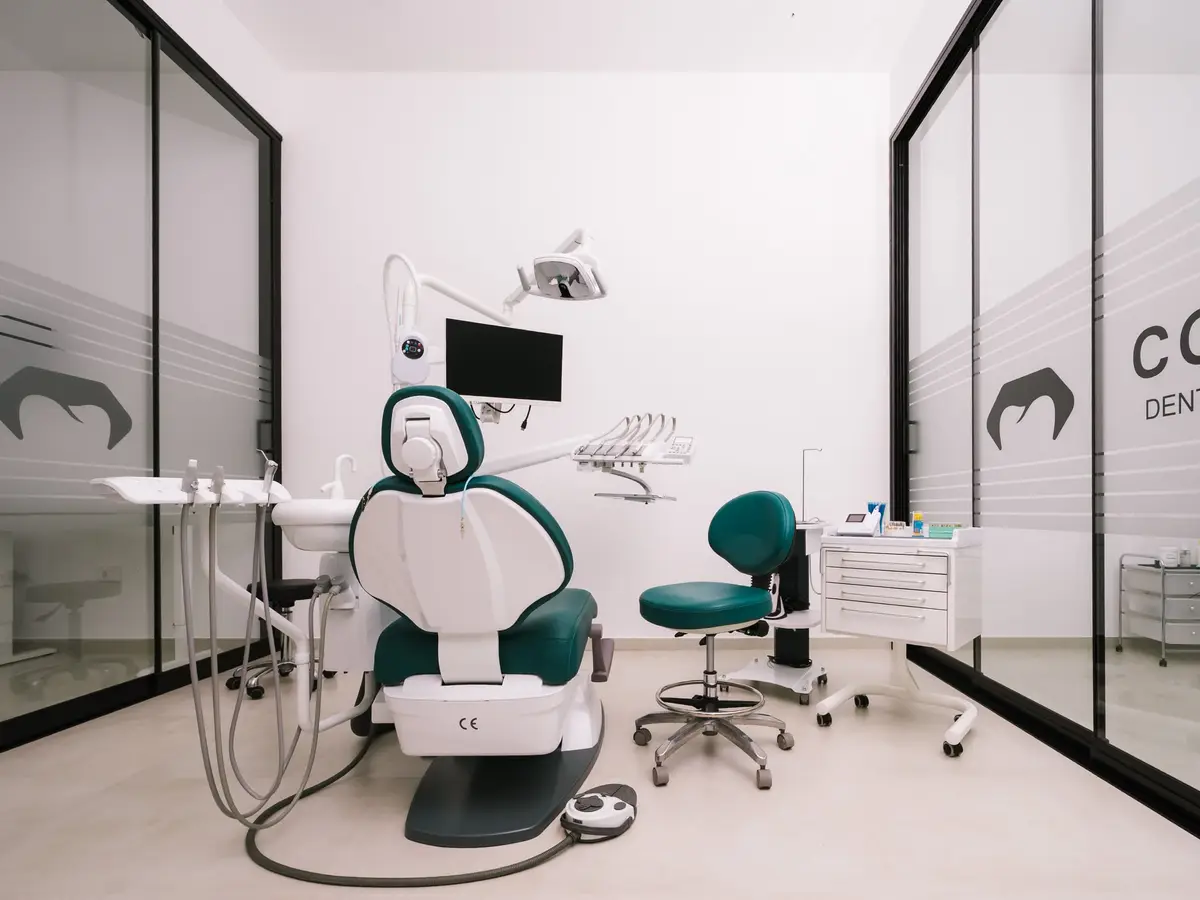 The general treatment room with a teal dental chair, between glass walls bearing the Confident logo